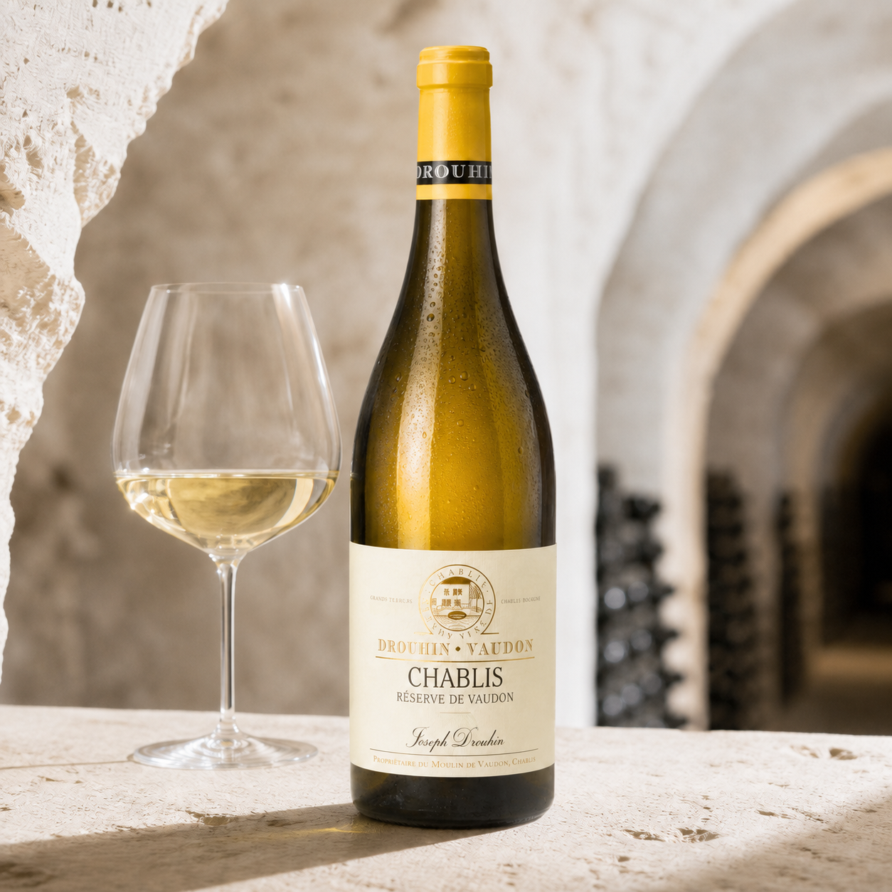 Joseph Drouhin Réserve de Vaudon Chablis 2025 bottle and pale-gold wine in a limestone cellar setting